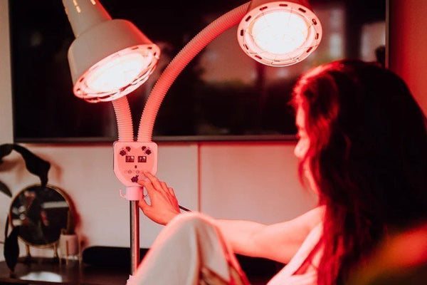 Vrouw stelt van dichtbij een infraroodlamp met twee koppen in, de kamer baadt in rood licht