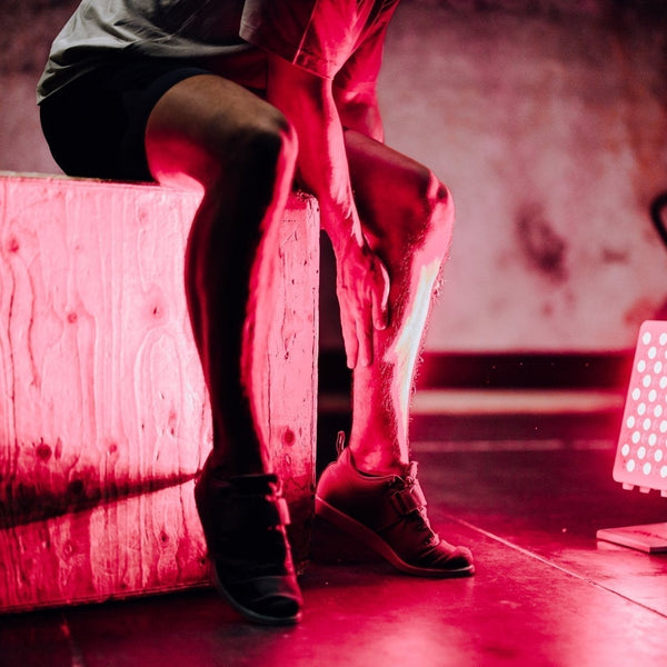 Sporter zit op een plyobox in de gym en wrijft over zijn kuit, rood licht paneel op de vloer