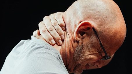 Man met bril grijpt naar zijn nek van de pijn, zoals bij fibromyalgie en chronische pijnklachten