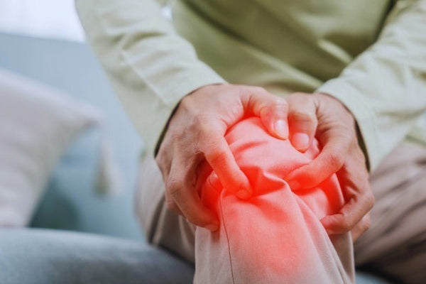 Oudere persoon op de bank houdt de knie vast, met een rode gloed die de pijn bij artrose aangeeft