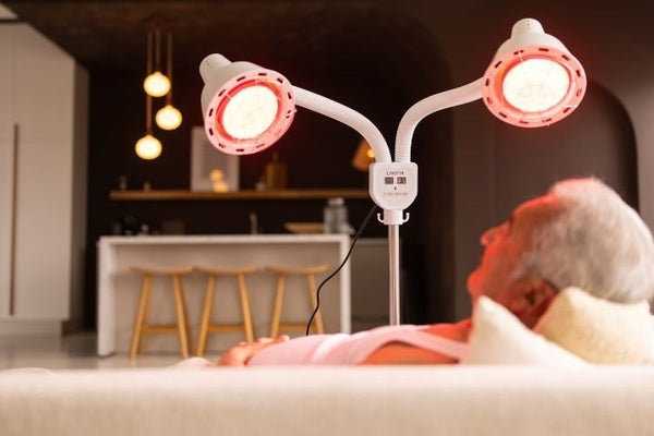 Man ontspant op de bank onder een staande infraroodlamp met twee rood gloeiende koppen