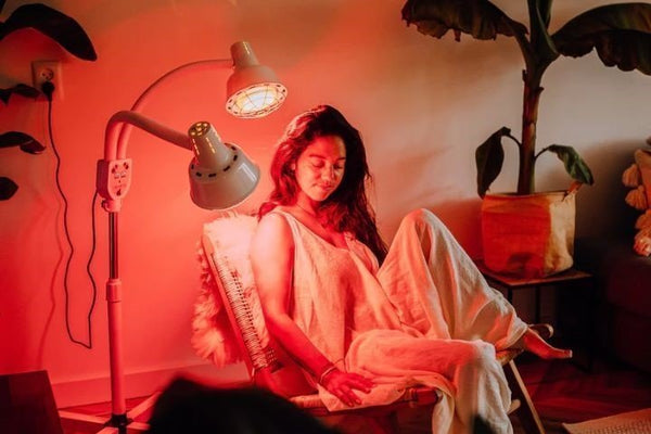 Vrouw met gesloten ogen krijgt rood licht therapie op haar gezicht van een infraroodlamp met twee koppen