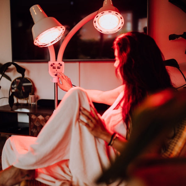 Vrouw in badjas zit in een stoel bij een infraroodlamp met twee verstelbare koppen