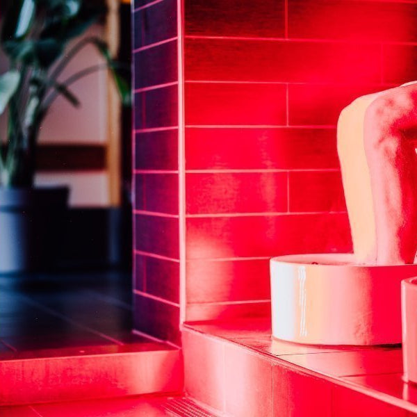 Smalle rode lichttherapielamp in een betegelde badruimte, man zit met voeten in een voetenbad