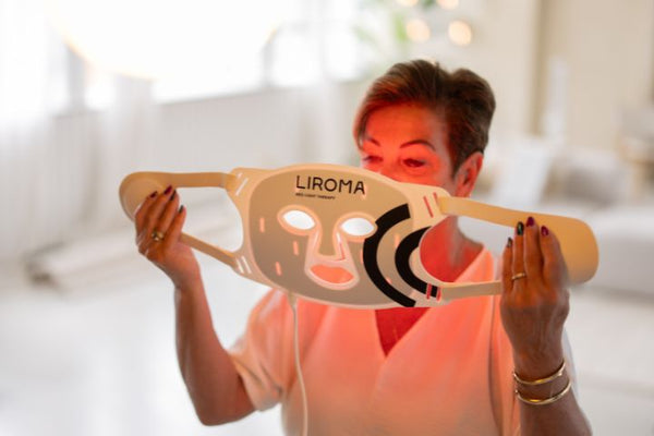 Vrouw houdt een verlicht LED-gezichtsmasker voor haar gezicht voor lichttherapie op de huid