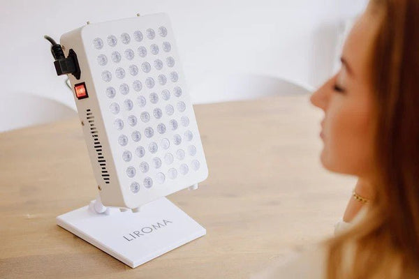 Wit Liroma paneel voor rood licht therapie op een tafelstandaard, gericht op het gezicht van een vrouw
