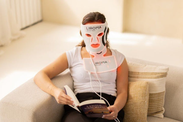Vrouw leest thuis op de bank met een LED-gezichtsmasker en halsband voor lichttherapie op