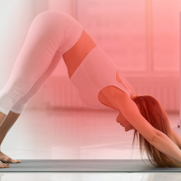 Vrouw in de neerwaartse hond op een yogamat naast een staand rood licht paneel, kamer in rood licht