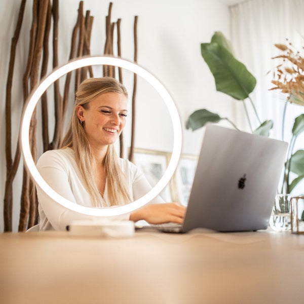 Lachende vrouw werkt aan haar laptop in het witte licht van een ronde daglichtlamp