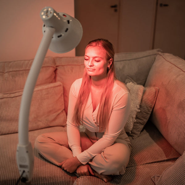 Vrouw zit in kleermakerszit op de bank met een infraroodlamp op een zwanenhals op haar gericht