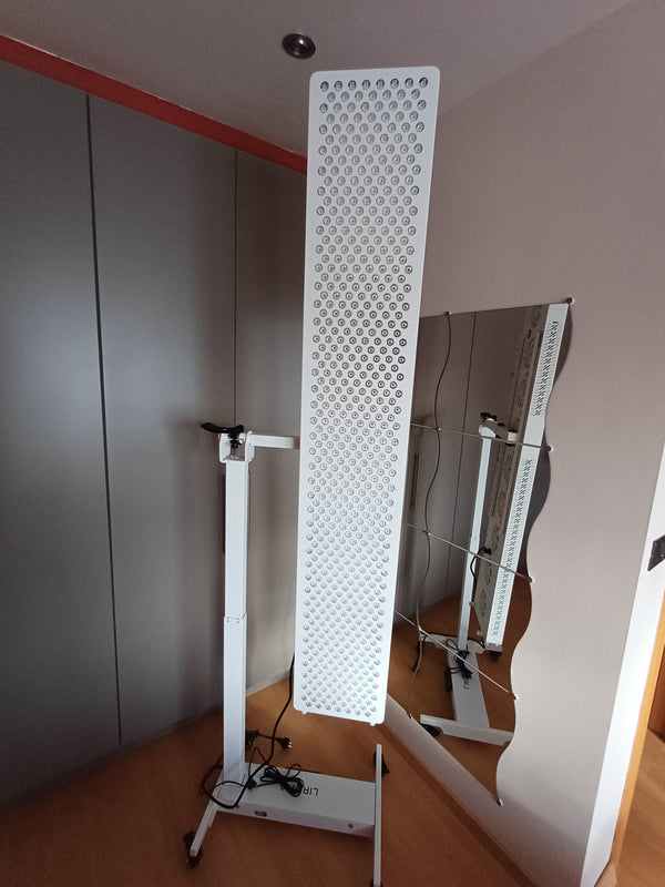 Hoog smal Liroma roodlichtpaneel op een verrijdbare standaard in een slaapkamer bij een spiegel