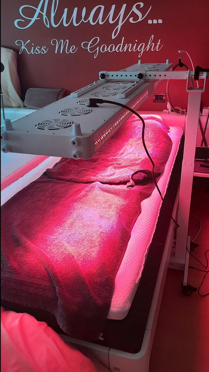 Behandelbed met een rood licht paneel erboven in een behandelruimte