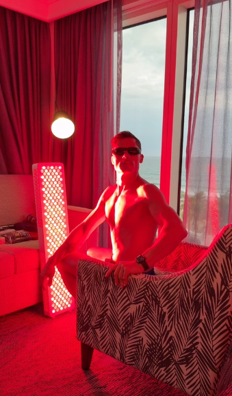 Man met beschermbril staat in een hotelkamer naast een staand Liroma roodlichtpaneel