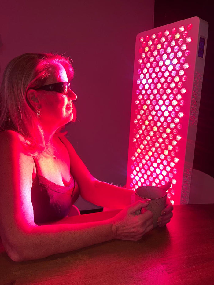 Vrouw met beschermbril naast een brandende rood licht therapie lamp aan tafel