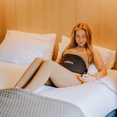 Vrouw ligt in bed met de Liroma HeatPULSE infrarood rugband om haar buik
