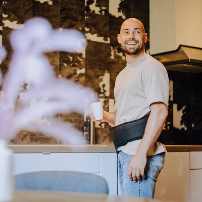 Man staat in de keuken met de Liroma HeatPULSE infrarood rugband om zijn onderrug