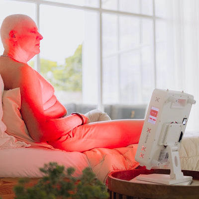 Man behandelt zijn rug op bed met de Liroma Compact rood licht lamp