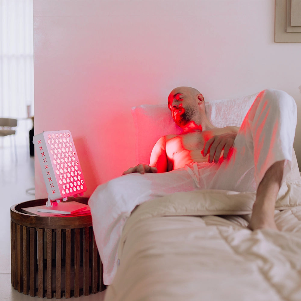 Man op bed naast de Liroma Compact rood licht lamp op het nachtkastje
