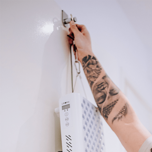 Hand hangt een roodlichtpaneel aan een plafondhaak met het PrimeFORCE Ophangsysteem
